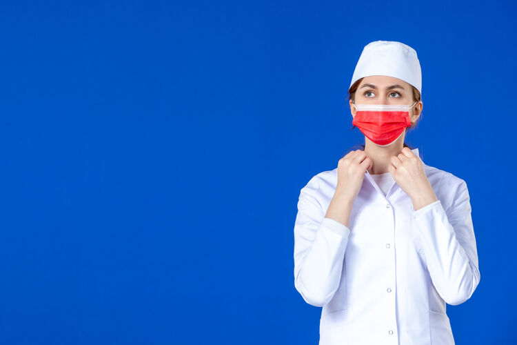 医学正面图蓝色墙上戴着红色面罩的年轻护士 穿着医疗服大流行视图人