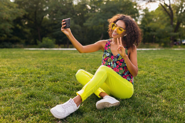 女性年轻时尚积极的黑人女性 自拍 戴着无线耳机听音乐 在公园里玩得很开心 夏日时尚 五颜六色的时髦装扮太阳镜欢呼享受