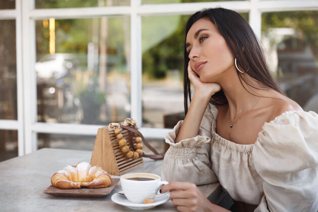 早餐时尚女士在咖啡馆里 喝着咖啡 倚在桌子上 欣赏着户外的景色放松白天羊角面包