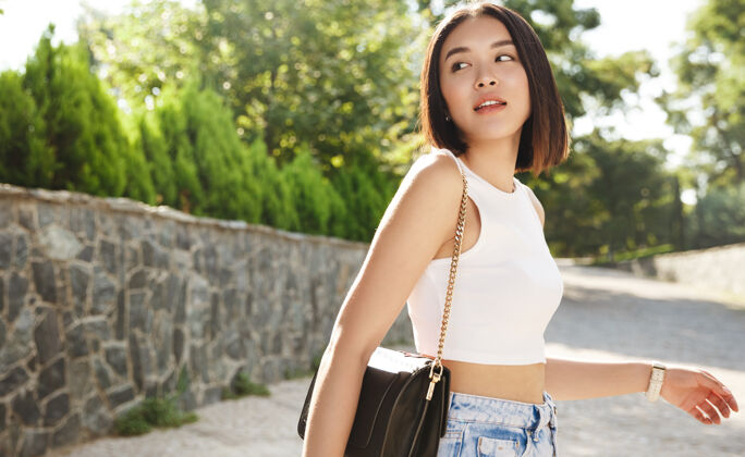 年轻年轻时尚的亚洲女人走在街上的画像 穿着时髦的服装 转过身来 看起来很体贴休闲花园公园