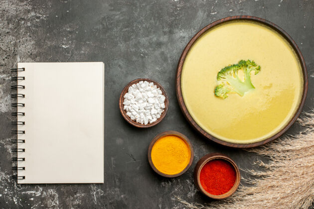 食物奶油西兰花汤在一个棕色的碗和不同的香料与笔记本在灰色的桌子上碗笔记本健康