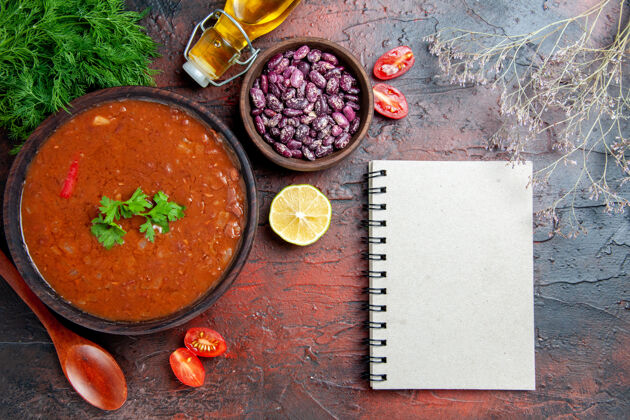 胡椒经典的番茄汤在一个棕色的碗里豆勺和笔记本上一瓶油混色桌上西红柿笔记本豆类