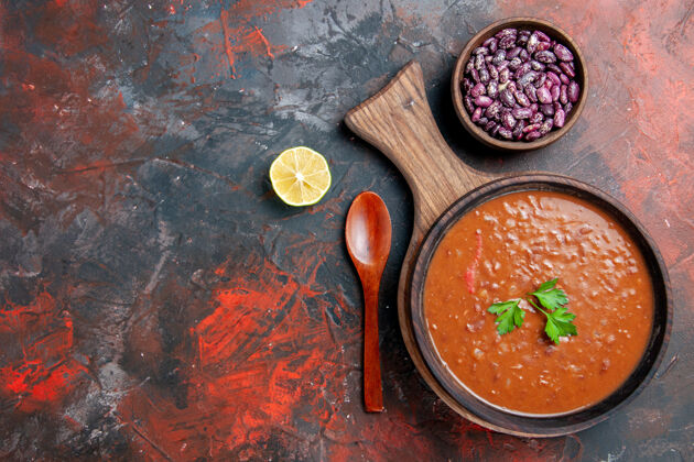 碗西红柿汤的水平视图在一张五颜六色的桌子上的砧板上掉落的油瓶豆搅拌汤晚餐