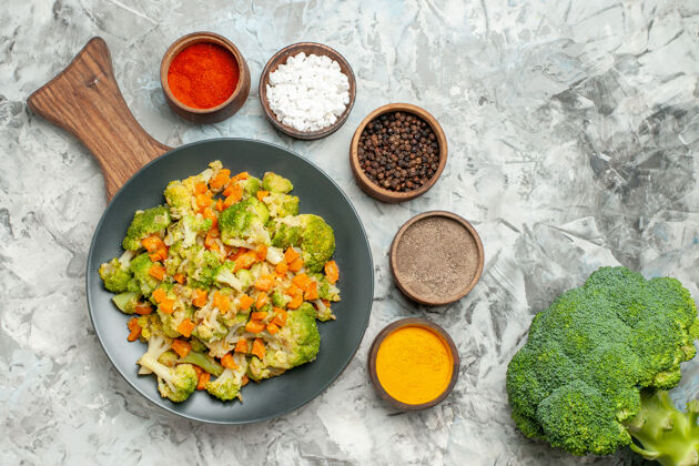 板新鲜健康的蔬菜沙拉放在木制的砧板上 香料放在白色的桌子上沙拉美食切割