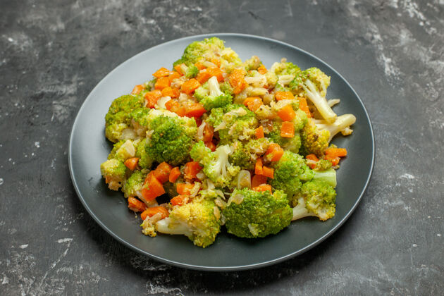午餐在灰色桌子上的黑色盘子上放半杯健康的西兰花和胡萝卜健康一半花椰菜