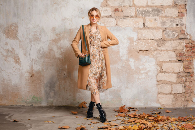 秋天穿着米色外套的迷人时尚金发女人在街上靠着老式的墙走着年轻姿势外套
