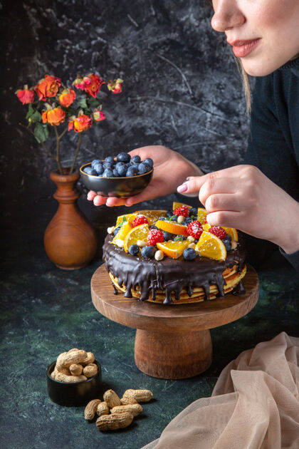 前面正面图美味的巧克力蛋糕得到装饰与新鲜水果的女性在黑暗的墙壁橘子巧克力视野