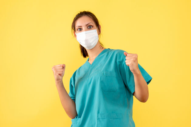 护士正面图黄色背景上穿着医用衬衫 带无菌面罩的女医生欢欣鼓舞外套正面欢喜