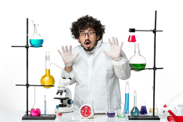 烧杯正面图身着特殊套装的年轻男性科学家站在桌子旁 白色桌子上摆着解决方案办公桌科学化学
