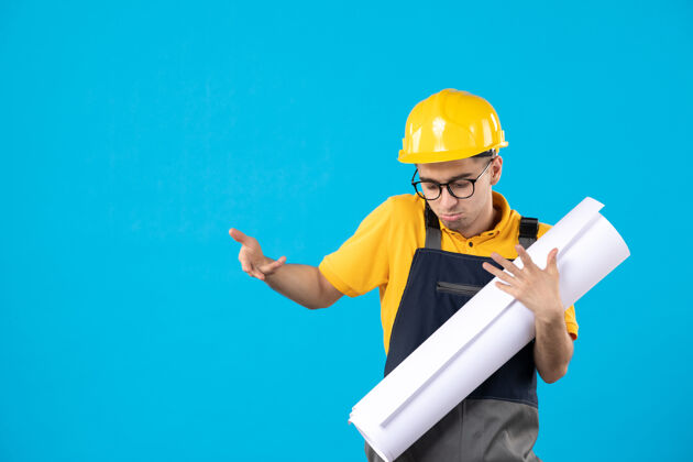 蓝色身穿黄色制服和头盔的男性建筑工人正视图 蓝色墙上有平面图人计划前面
