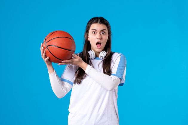 篮球正面图：蓝色墙上挂着篮球的年轻女子比赛成人正面