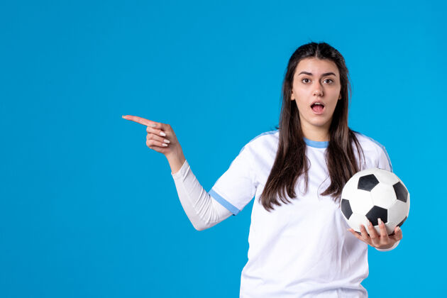 视图前视图：蓝色墙上有足球的年轻女性足球成人指向