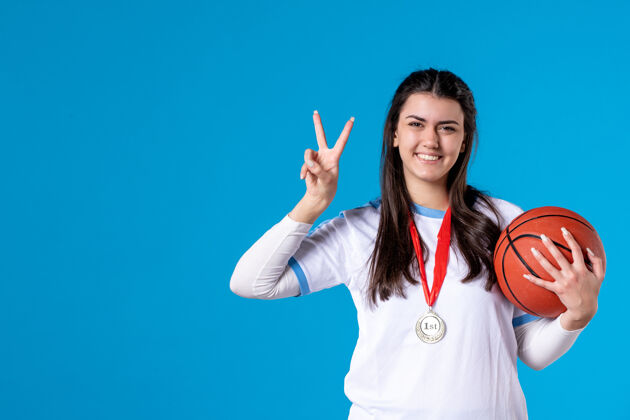 比赛正面图：年轻女子拿着篮球站在蓝色的墙上女人青年体育