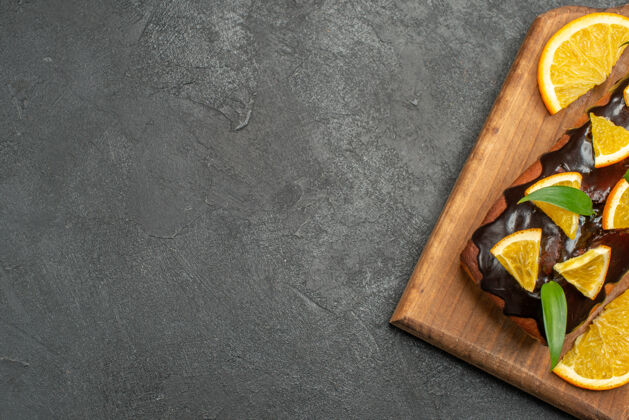 陷阱在黑桌子的砧板上放上半张柠檬和巧克力装饰的美味蛋糕木头板巧克力