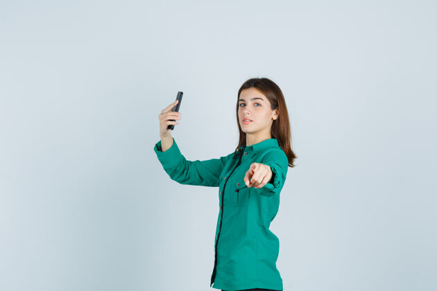 手机一张年轻女士在手机上自拍的照片 她穿着绿色衬衫 指着相机 看起来很自信华丽专业人物