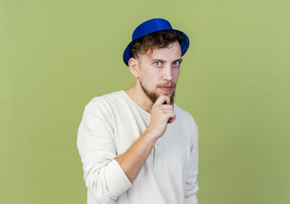 手体贴的年轻帅哥斯拉夫党人戴着党帽看着相机把手放在下巴上橄榄绿的背景与复制空间隔离年轻党空间