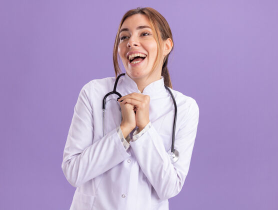 兴奋兴奋地看着身边年轻的女医生穿着医用长袍手牵听诊器隔离在紫色的墙上医疗壁板穿