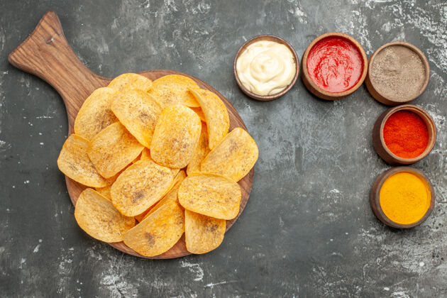 可食用水果上图：灰色桌子上的木制砧板上放着薯片 香料和蛋黄酱 还有番茄酱零食木材食品