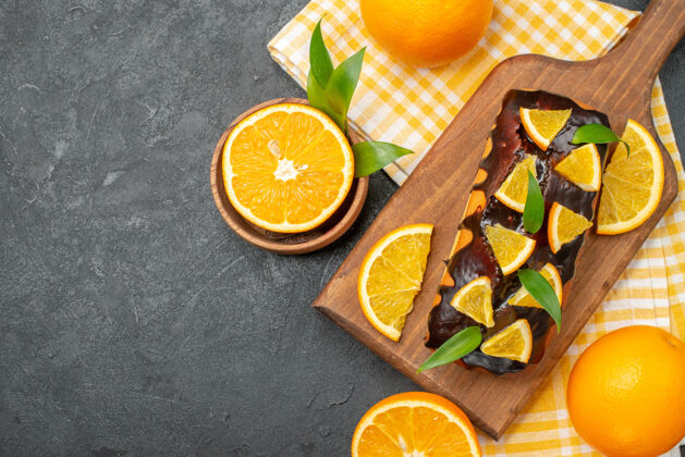 甜橙在黑暗的桌子上俯瞰整个软蛋糕和带叶子的切橘子深色水果饮食