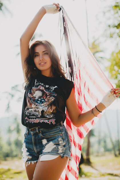 年轻带着美国国旗的年轻性感女人日落自然度假