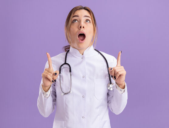 点惊讶地抬头看了看年轻的女医生 穿着医用长袍 用听诊器指着隔离在紫色墙上的上面听诊器医疗长袍