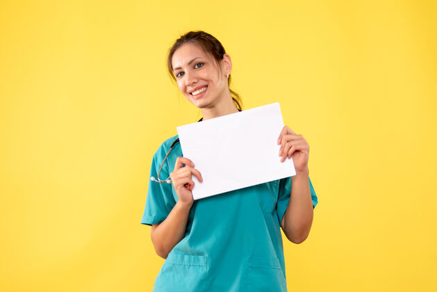 持有正面图黄色背景下穿着医疗衫的女医生拿着纸分析纸黄色女医生