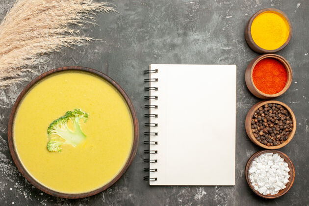 午餐奶油西兰花汤在一个棕色的碗和不同的香料旁边的笔记本在灰色的桌子上一餐蔬菜西兰花汤
