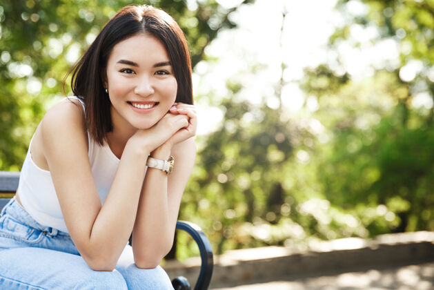 黑发美丽的亚洲女人坐在长椅上微笑着花园时尚无忧无虑