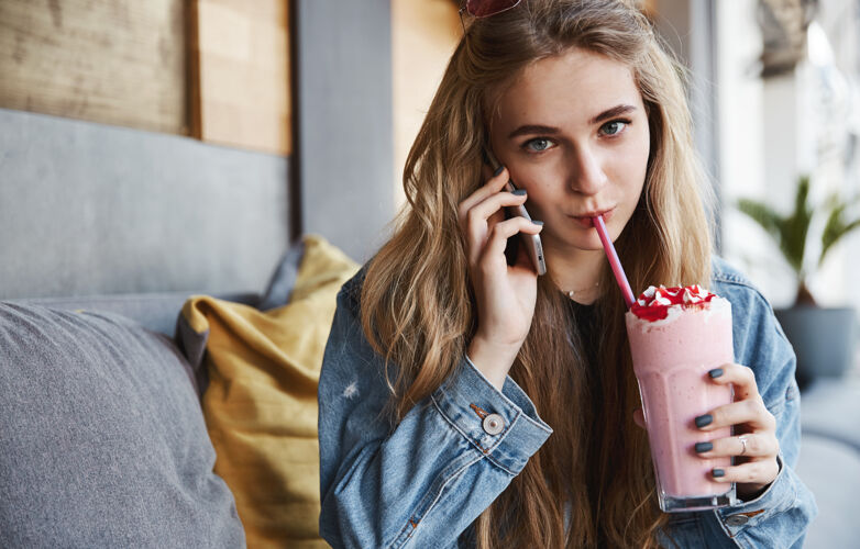 休息漂亮的金发女孩坐在咖啡馆里喝着冰沙 说话人脸城市