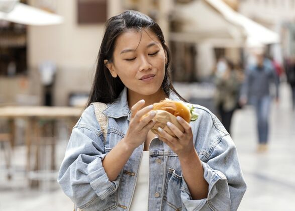 垃圾食品快乐的亚洲女人在户外吃汉堡饥饿街头食品快餐