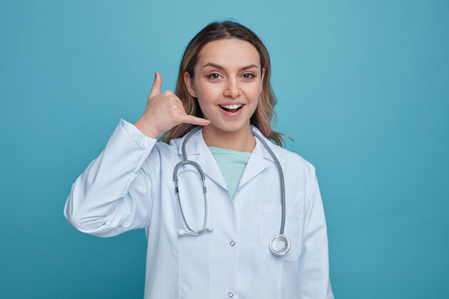 长袍兴奋的年轻女医生穿着医用长袍 脖子上戴着听诊器做着呼叫手势佩戴兴奋女性
