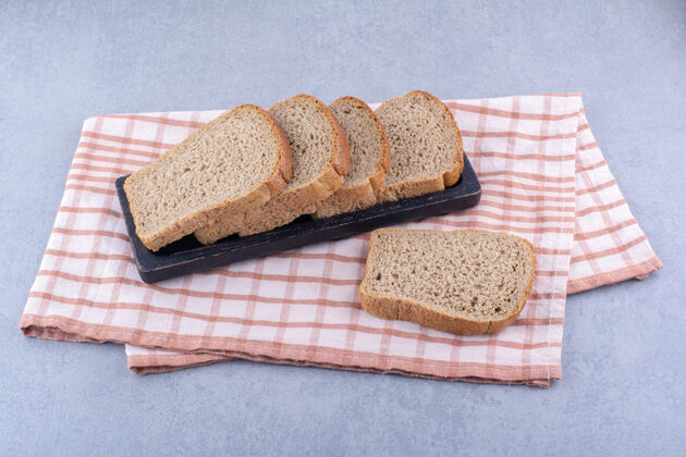 饮食在大理石表面的折叠毛巾上放一盘黑色的棕色切片面包烘焙食品面包酵母