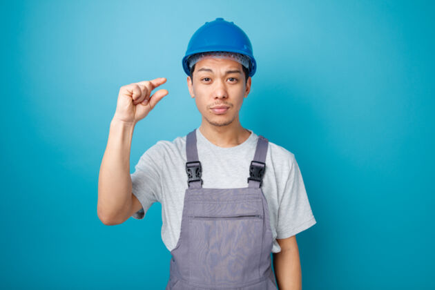 量皱眉的年轻建筑工人戴着安全帽和制服做着小动作小工人穿