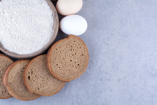 面包把黑面包和鸡蛋片放在大理石表面的一碗面粉上切片面团面粉