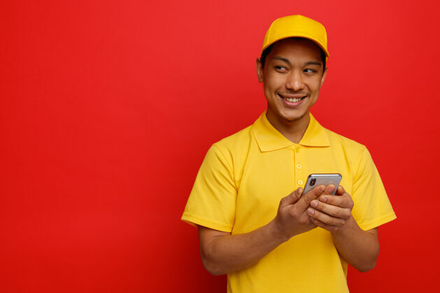 手机面带微笑的年轻送货员戴着帽子和制服拿着手机看着身边复印制服空格