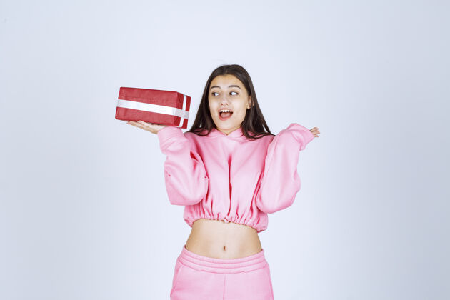 女性穿着粉色睡衣的女孩手里拿着一个红色长方形礼盒 看上去很满意年轻促销成人