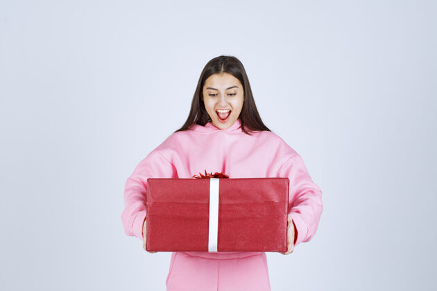 员工穿着粉色睡衣的女孩抱着一个大大的红色礼盒 微笑着庆祝服装人类