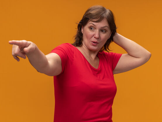 中间一位身穿红色t恤的中年妇女 手放在头上 用食指指着站在橙色墙上的东西站手指年龄