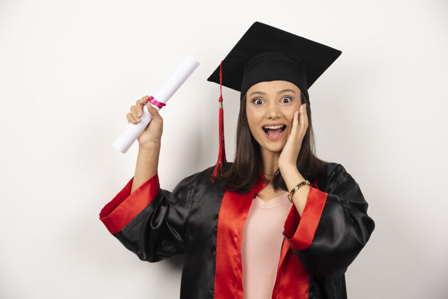 毕业大学毕业的女学生在白色的背景下穿着长袍感到快乐帽子帽子大学
