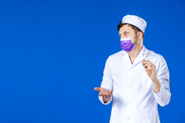 套装身穿医疗服 戴着紫色口罩的男医生正对着蓝色的脸拿着针剂注射男医生大流行