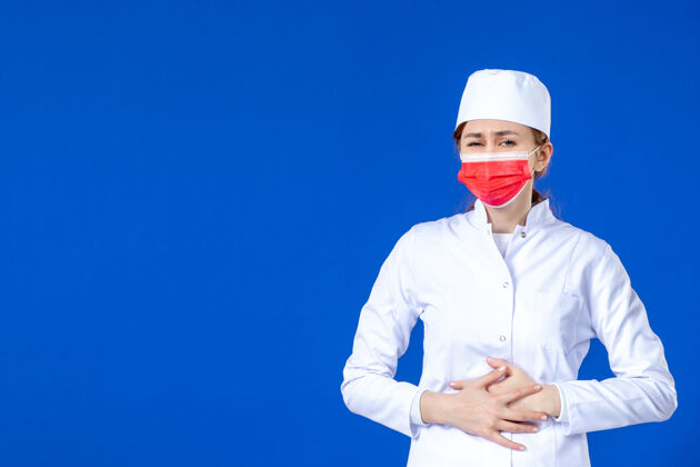 疾病身穿医疗服的年轻护士的正视图 蓝色的面具上有红色的面具年轻护士医学帽子