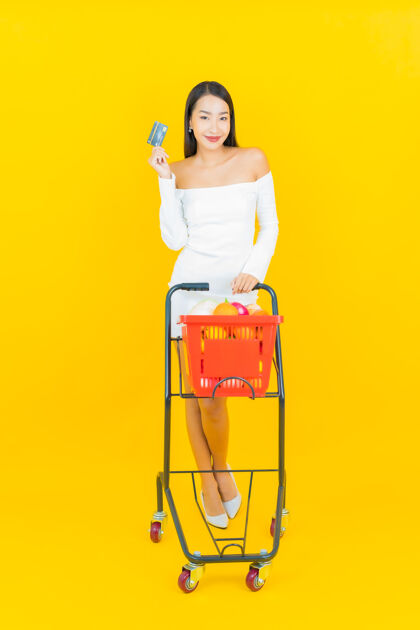 恐惧一幅美丽的亚洲年轻商业女性的画像 她拿着购物篮 从黄色墙上的超市拿着杂货买家商场女人
