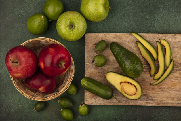 顶视图在木制的厨房板上放着熟透的新鲜鳄梨切片 桶上放着红苹果 绿色的表面上隔离着酸橙和青苹果配料切片新鲜