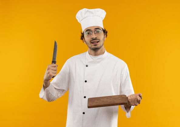 制服年轻的男厨师穿着厨师制服 戴着眼镜 手里拿着刀和砧板切割年轻刀