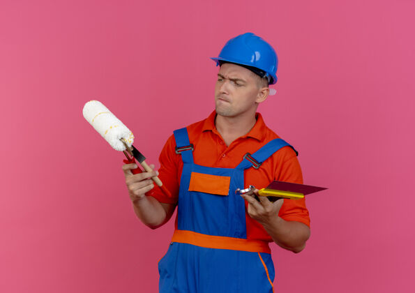 制服迷茫的年轻男建筑工人穿着制服 戴着安全帽 拿着看建筑工具安全男性佩戴