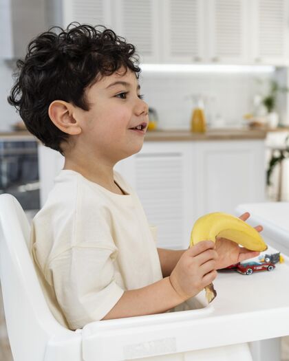 可爱可爱的小男孩在幼儿椅上吃早餐的画像香蕉餐桌早餐
