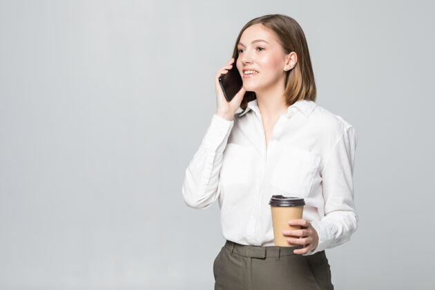 女性一个年轻的女商人拿着一杯咖啡和一部电话 隔着一片白色食物沟通说话