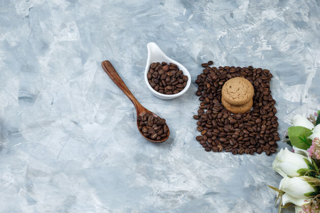 卡布奇诺把咖啡豆放在木勺里 白色瓷壶里放着饼干 浅蓝色大理石背景上放着花水平杯子味道意式咖啡