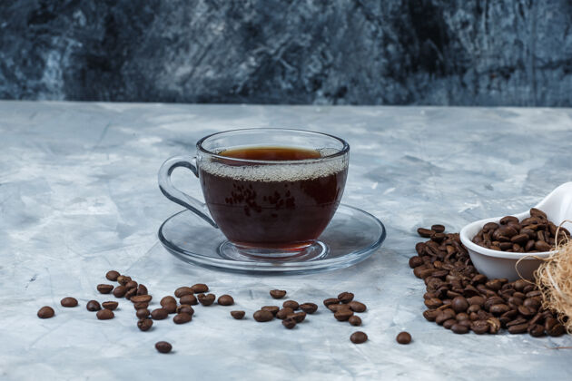 讨论在深蓝色和浅蓝色大理石背景上 用一杯咖啡将咖啡豆放在白色瓷罐中 水平放置早餐豆子乐趣