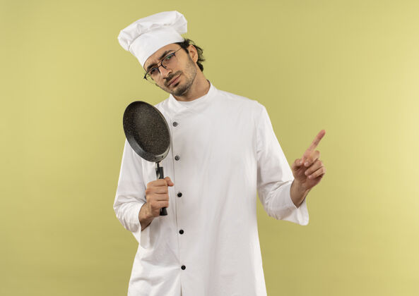穿年轻的男厨师穿着厨师制服 戴着眼镜 手里拿着煎锅 指着旁边眼镜年轻持有